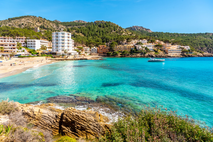 Sandbucht von Sant Elm mit türkisfarbenem Wasser, Hotels am Hang und Blick auf die umliegenden Berge