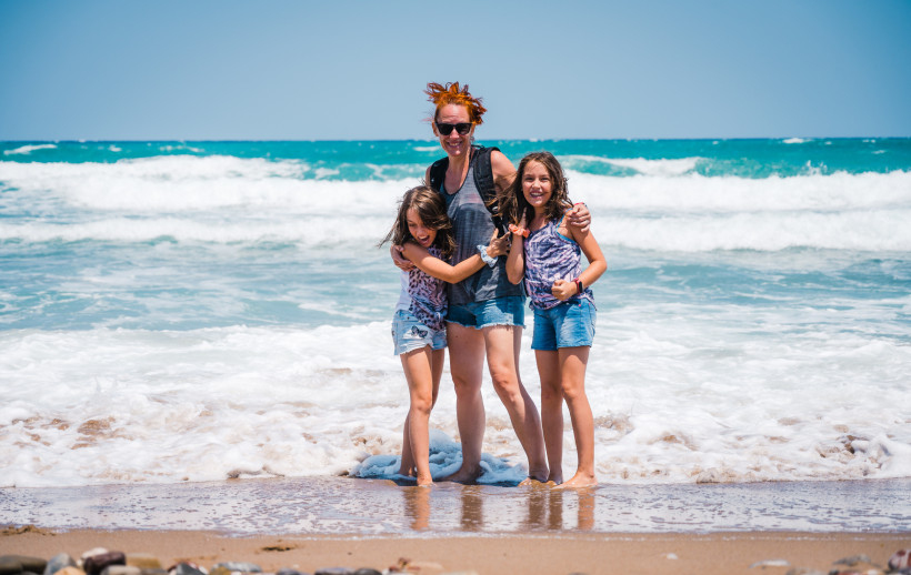 Frau mit zwei Kindern am Strand von Malia, im Hintergrund Wellen und Meer