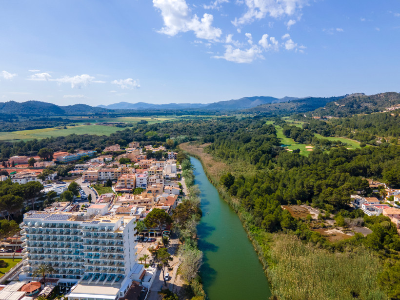 Luftaufnahme von Canyamel mit Flusslauf Torrent de Canyamel und grüner Landschaft im Hintergrund
