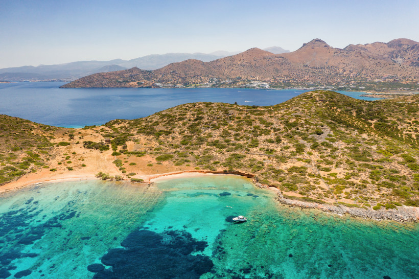 ruhige Bucht bei Elounda Bucht bei Elounda mit türkisfarbenem Wasser, kleinem Boot und hügeliger Küstenlandschaft