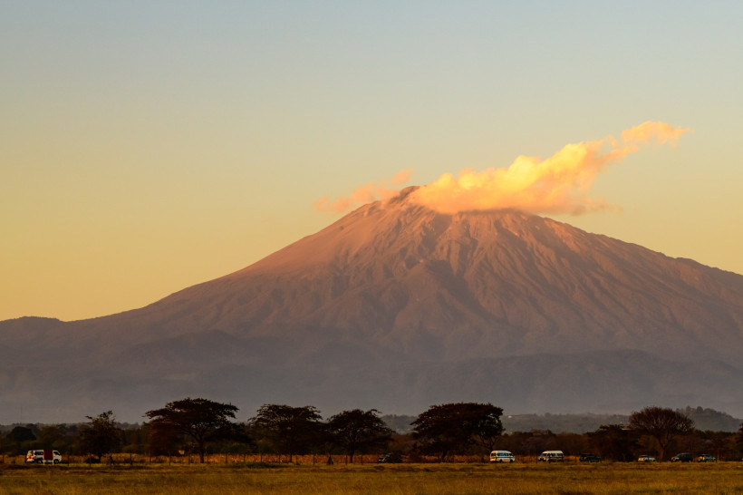 Mount Meru bei Sonnenuntergang mit Wolke am Gipfel, davor Savannenlandschaft mit Bäumen