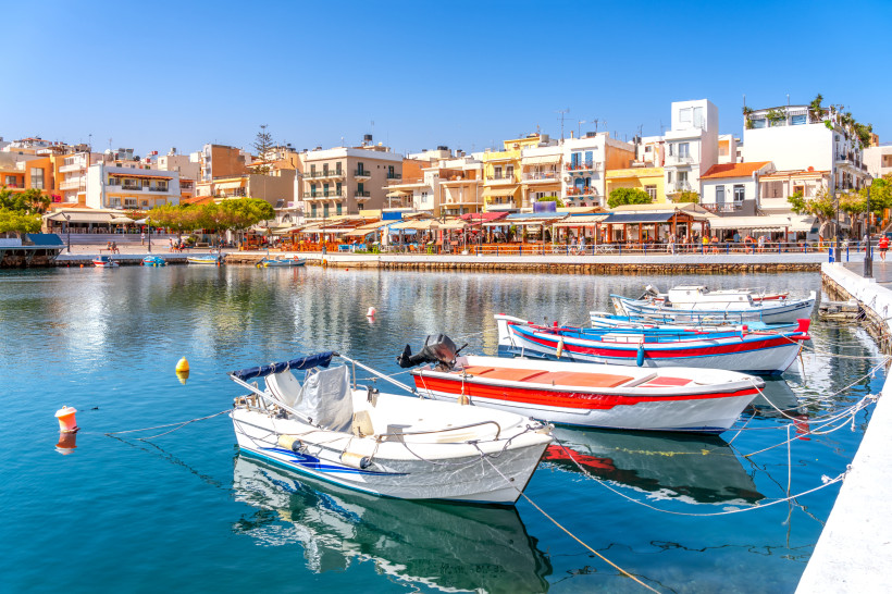 Hafen von Agios Nikolaos mit kleinen Booten im Vordergrund und Uferpromenade mit Gebäuden im Hintergrund