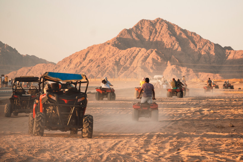 Gruppe von Fahrern auf Quads und Buggys unterwegs durch die weite Wüstenlandschaft mit Bergen im Hintergrund