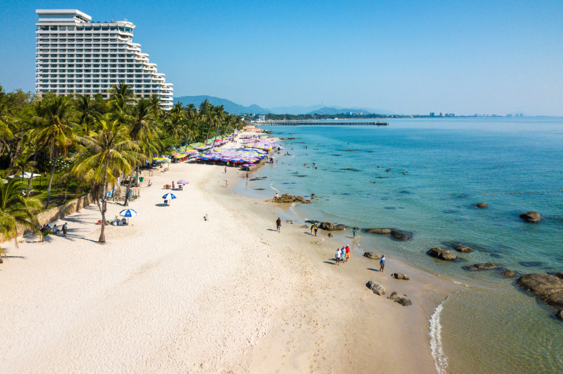 Breiter Sandstrand mit Palmen und Hotel am Meer in Hua Hin, Thailand – beliebtes Reiseziel für Badeurlaub