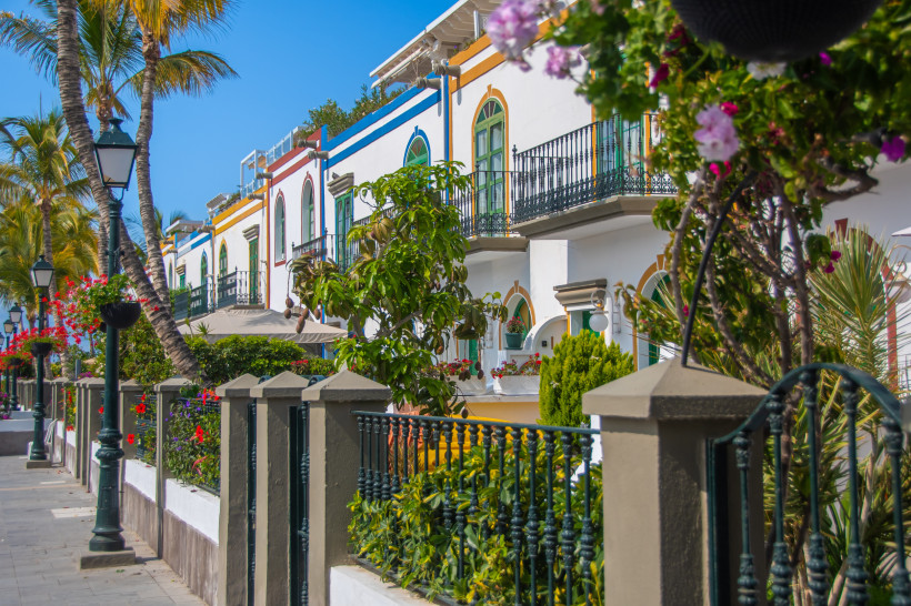 Weiße Häuser mit bunten Fensterrahmen und Balkonen in Puerto de Mogán auf Gran Canaria, umgeben von Palmen und Blumen