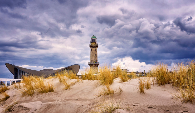 Warnemünde: Leuchtturm und Teepott an der Küste Leuchtturm Warnemünde und Teepott hinter Sanddünen unter wolkigem Himmel