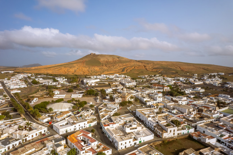 Luftaufnahme von Teguise auf Lanzarote mit weißen Häusern und dem Castillo de Santa Bárbara auf einem Hügel im Hintergrund.