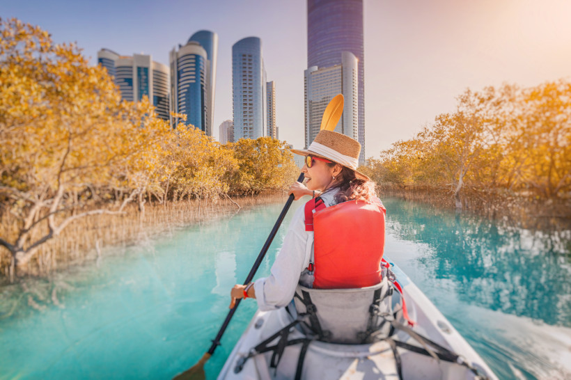 Frau paddelt im Kajak durch die Mangroven von Abu Dhabi mit Blick auf die Skyline