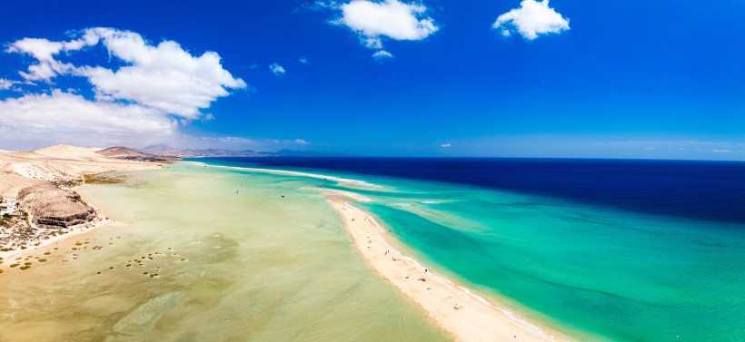 Sonne über Strand und Sandbank auf Fuerteventura Sonniger Strand auf Fuerteventura mit türkisfarbenem Meer und Sandbank unter blauem Himmel