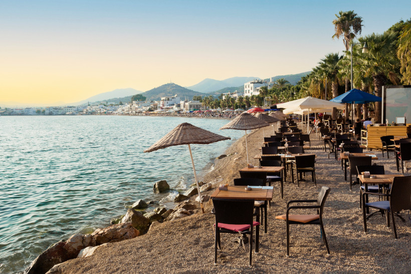 Strandpromenade in Bodrum mit Tischen, Sonnenschirmen, Palmen und Blick auf das Meer bei Abendlicht