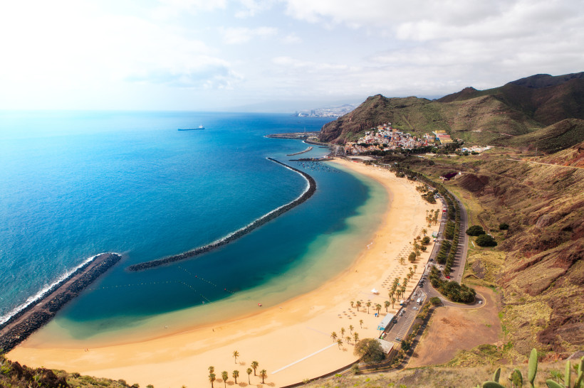 Luftaufnahme der Playa de las Teresitas auf Teneriffa mit hellem Sandstrand, Wellenbrechern und Küstenstraße