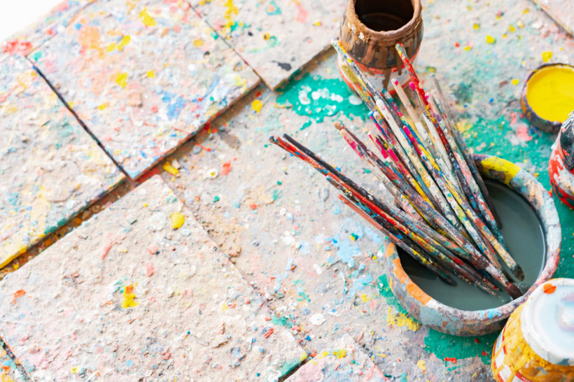 Ägypten - Hurghada Ein bunter Malplatz mit vielen mit Farbe bedeckten Pinseln in einem Becher, Farbdosen und Farbspritzern auf dem Untergrund. Alles wirkt kreativ-chaotisch und lebendig.