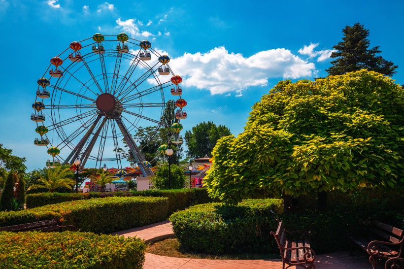 Bulgarien Großes Riesenrad in einem Freizeitpark am Meer, umgeben von gepflegten Gärten, Bäumen und Parkbänken. Der Himmel ist blau mit einigen weißen Wolken