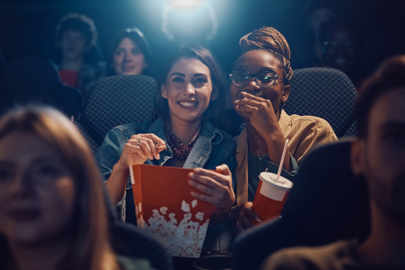 Ägypten - Sharm el Sheikh Zwei Frauen sitzen lachend im Kino, die vordere hält eine große Box Popcorn, die andere einen Softdrink. Sie schauen gespannt nach vorn, während im Hintergrund weitere Zuschauer zu sehen sind