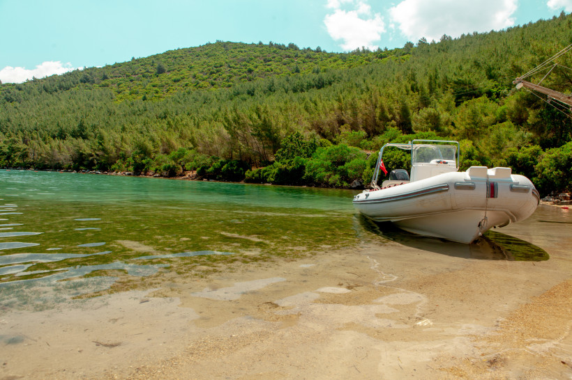 Kleines Motorboot liegt am sandigen Ufer einer ruhigen, grünen Lagune vor bewaldeten Hügeln