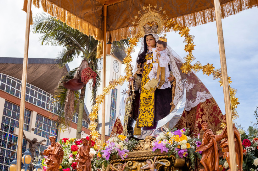 Fiesta Virgen del Mar Religiöse Prozession mit kunstvoll geschmückter Marienstatue, die das Jesuskind trägt, unter einem Baldachin vor einer Kirche mit Palmen im Hintergrund