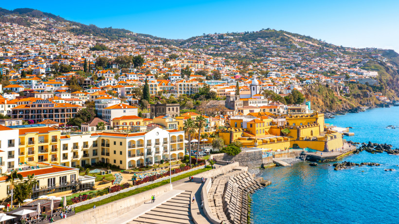 Blick auf die Altstadt von Funchal auf Madeira mit bunten Häusern, Hafenpromenade und Atlantikküste bei Sonnenschein