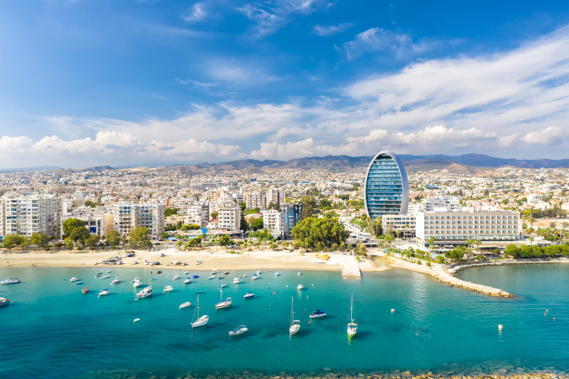 Panoramablick auf Limassol mit Strand, Segelbooten und dem markanten Oval Tower an der Küste.
