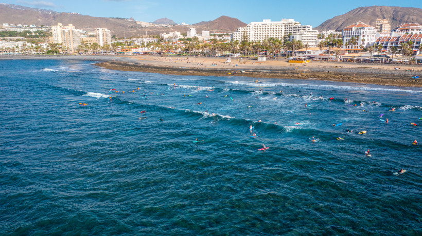 Surferparadies auf Teneriffa – Playa de las Américas Viele Surfer im Meer vor Playa de las Américas auf Teneriffa. Wellen, Strandpromenade und Hotels im Hintergrund. Beliebter Surfspot der Insel.
