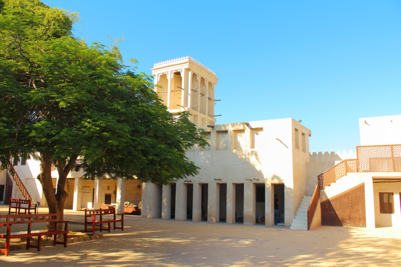 Innenhof des Nationalmuseums Ras Al Khaimah mit traditioneller Architektur, Windturm und schattenspendendem Baum.