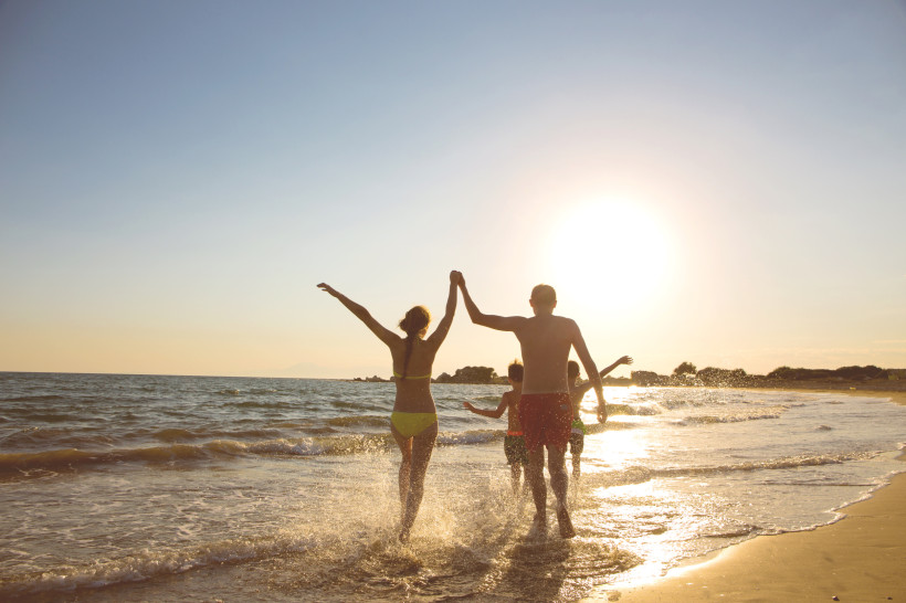 Familie mit Kindern läuft bei Sonnenuntergang durch das Meer am Strand von Side in der Türkei