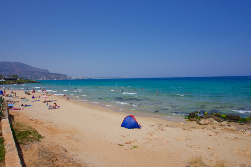 Sandstrand in Malia mit Badegästen, seichtem Wasser und kleiner Strandmuschel am Ufer