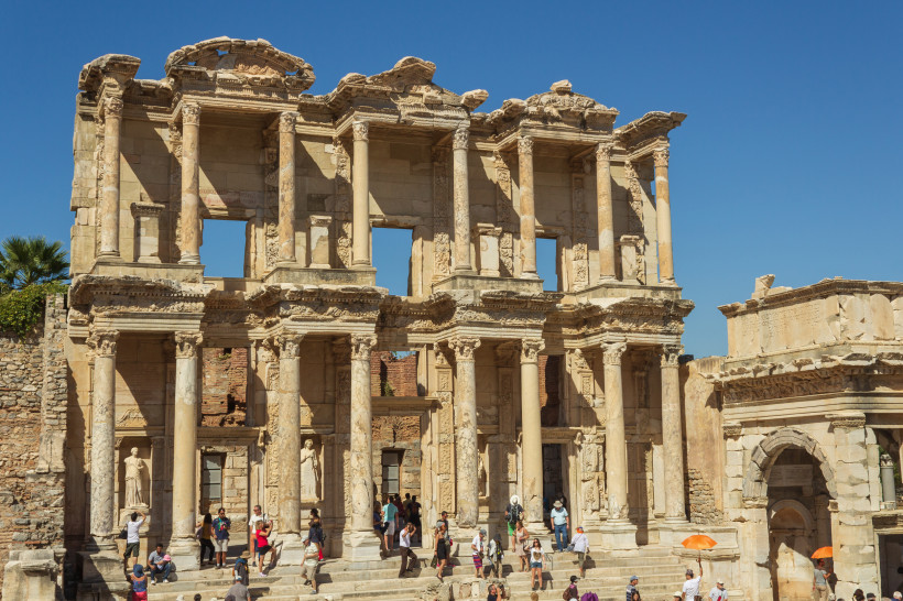 Die Fassade der antiken Celsus-Bibliothek in Ephesos, Türkei. Die gut erhaltene römische Ruine mit ihren hohen Säulen und Statuen zieht zahlreiche Besucher an, die auf den Stufen stehen und das Bauwerk bewundern.