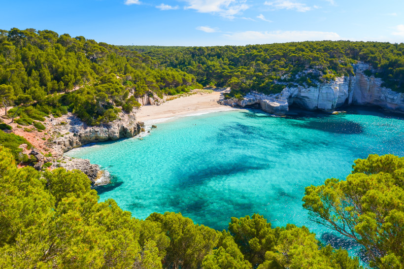 Naturbucht auf Menorca mit klarem Wasser, Felsen und Pinien