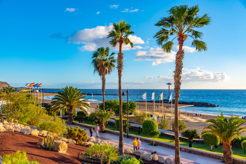 Palmen und Uferpromenade an der Playa de Las Vistas mit Blick auf Strand und Atlantik