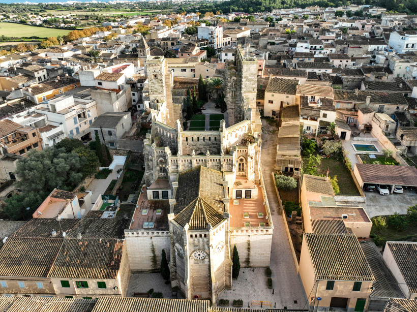 Luftaufnahme einer historischen Altstadt auf Mallorca mit großer Natursteinkirche, Uhrturm, engen Gassen und typischen Häusern mit Ziegeldächern