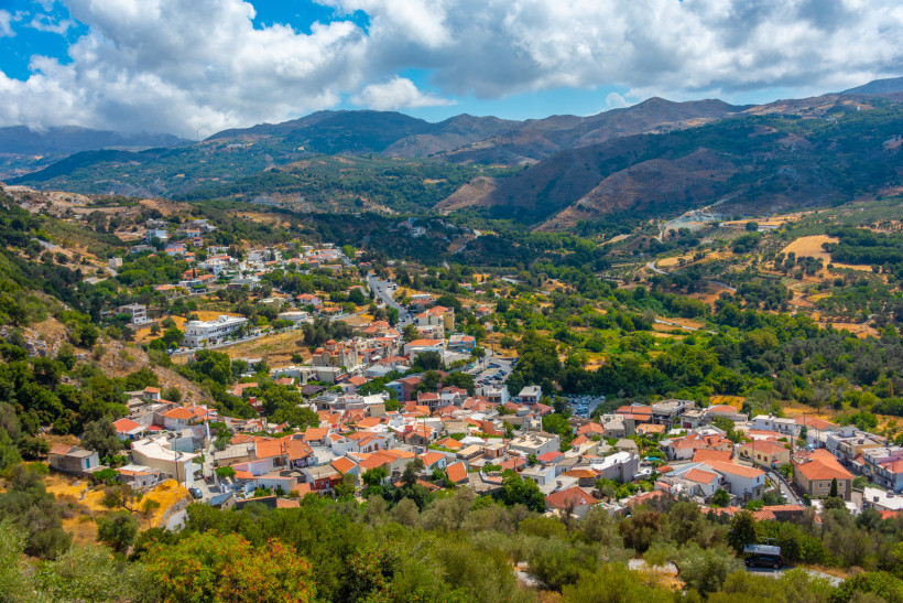 Kreta für Entdecker: Blick auf ein Bergdorf auf Kreta mit Olivenhainen und Gebirgslandschaft Bergdorf auf Kreta in einem grünen Tal mit Olivenhainen und Bergen unter wolkigem Himmel
