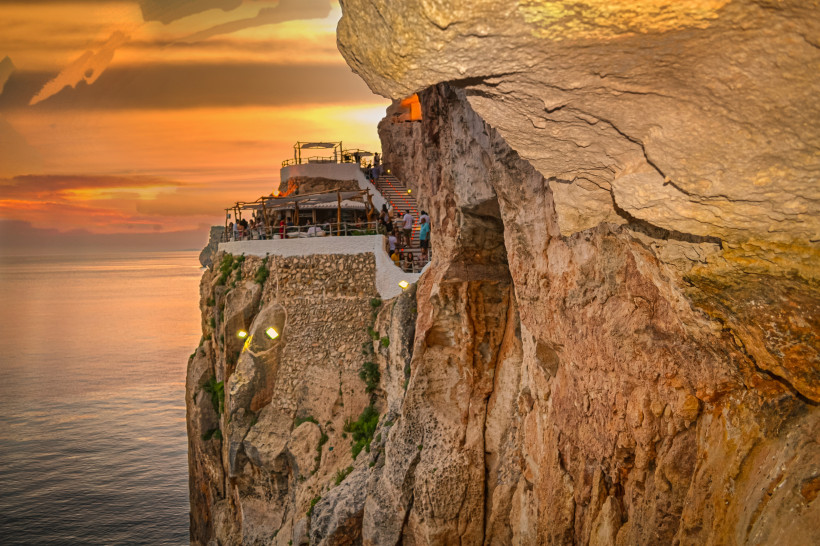 Terrassenanlage der Cova d'en Xoroi an einer Steilklippe über dem Meer bei Sonnenuntergang, Menorca