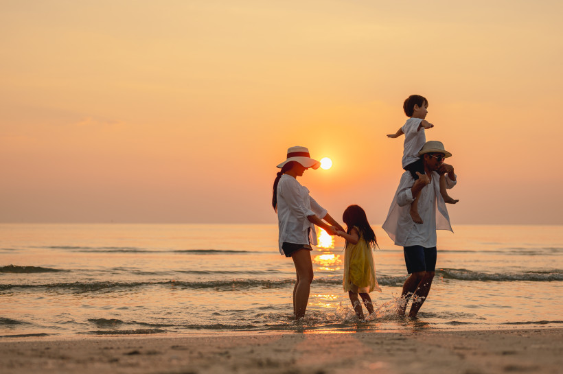 Familienmoment am Strand im goldenen Licht des Sonnenuntergangs Familie spielt im seichten Wasser am Strand während eines warmen Sonnenuntergangs