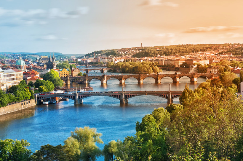 Prag Panorama von Prag mit Moldau und mehreren Brücken, darunter die Karlsbrücke; Altstadtdächer, Türme und viel Grün im warmen Licht.