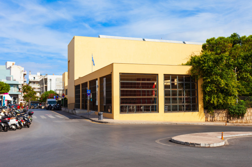 Außenansicht des Archäologischen Museums Heraklion mit modernem, gelbem Gebäudekomplex an einer Straßenkreuzung