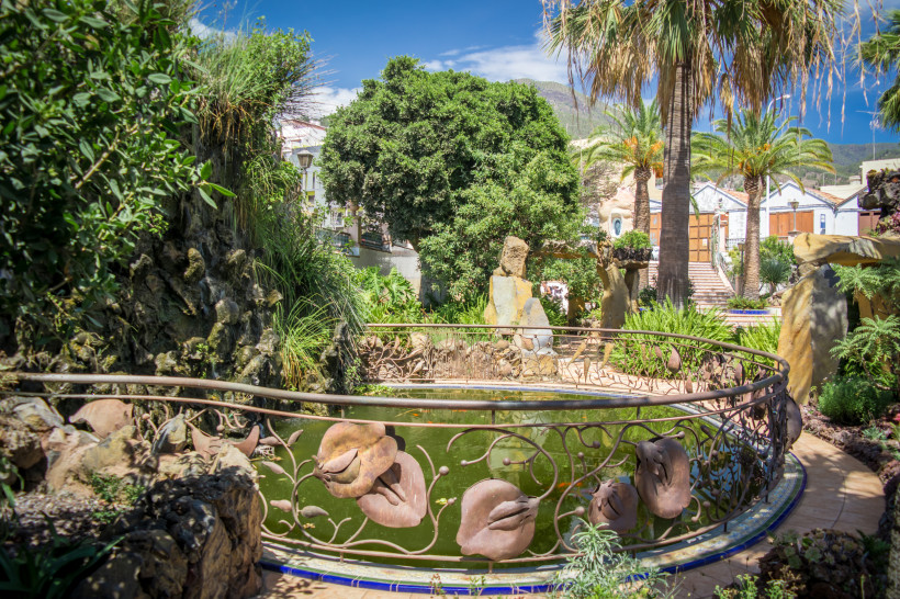 Gartenanlage mit Teich und Palmen in Los Llanos Gartenanlage in Los Llanos mit kleinem Teich, Geländer mit Metallblumen, Palmen und üppiger Vegetation