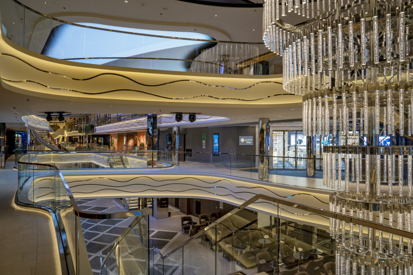 Mehrstöckige World Gallery an Bord der MSC World Europa mit geschwungenen Galerien, Rolltreppen und großem Kronleuchter