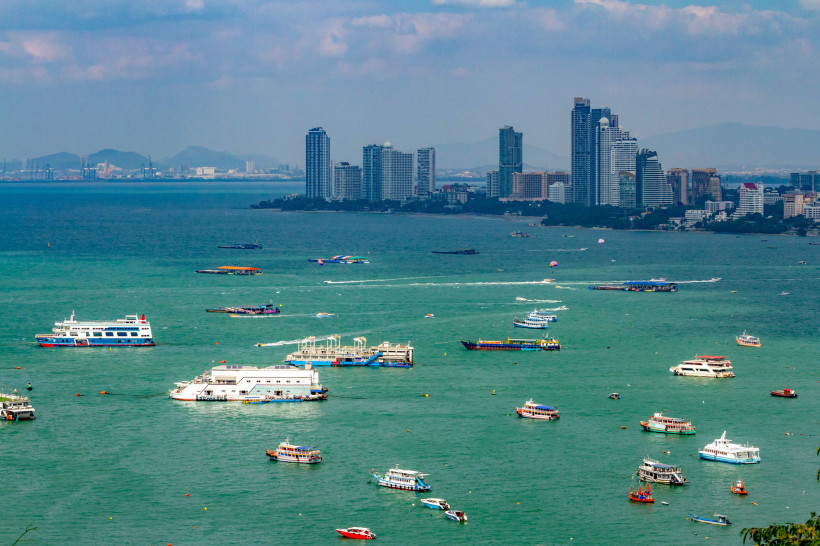 Blick auf die Küste von Pattaya mit zahlreichen Ausflugsbooten und Hochhäusern Verschiedene Boote auf dem Meer vor der Skyline von Pattaya mit modernen Hochhäusern und grünen Bergen im Hintergrund