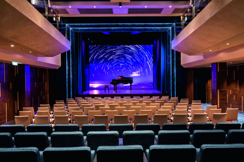 Showbühne an Bord der Mein Schiff 1 mit Flügel vor LED-Hintergrund und Sitzreihen im Zuschauerraum