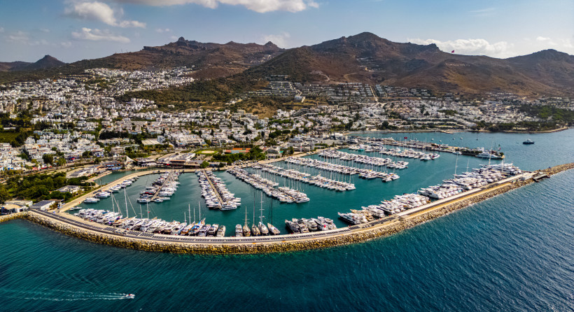 Luftaufnahme einer großen Marina mit zahlreichen Yachten, Hafenmole und Küstenstadt vor bergiger Landschaft