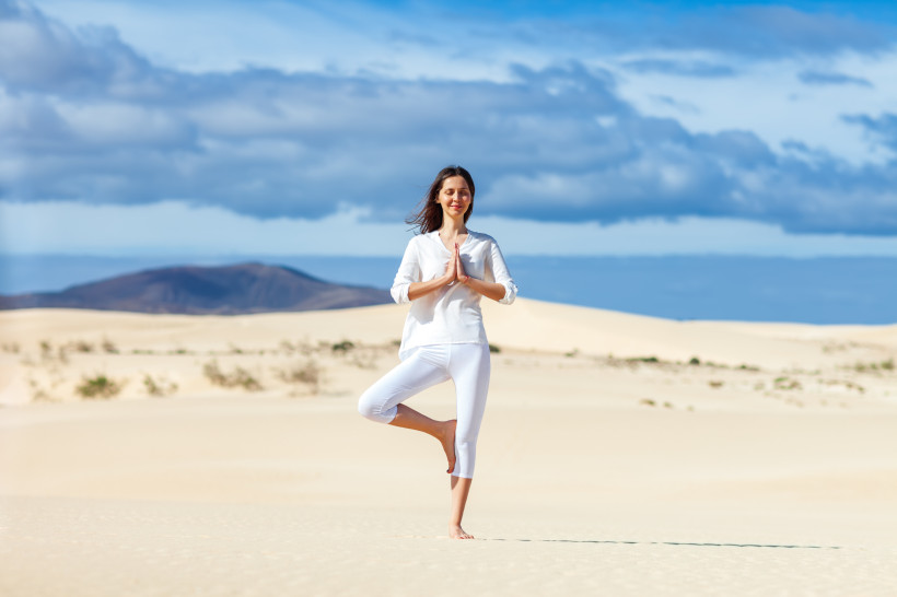 Yoga in den Dünen von Fuerteventura – Entschleunigung inmitten der Natur Frau praktiziert Yoga in den Dünen von Fuerteventura mit Blick auf die weite Landschaft und den blauen Himmel