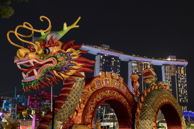 Singapur Farbenfrohe Drachenfigur mit großen Zähnen und bunten Schuppen im Vordergrund. Dahinter moderne Hochhäuser bei Nacht, darunter das beleuchtete Marina Bay Sands Hotel in Singapur. Die Szene zeigt eine festliche Dekoration zum chinesischen Neujahrsfest.