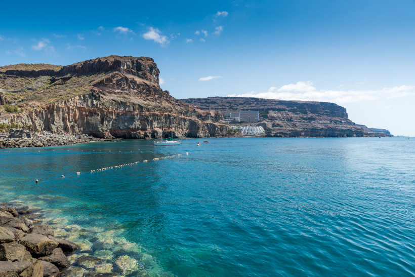 Puerto de Mogán – Küstenansicht bei Playa de Mogán mit Klippen und ruhigem Meer Blick auf die Küste bei Playa de Mogán in Puerto de Mogán mit felsigen Klippen und blauem Meer
