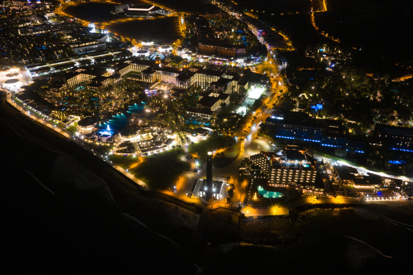 Nachtaufnahme aus der Luft vom Lopesan Costa Meloneras Bereich mit beleuchteter Hotelanlage, Promenade und Leuchtturm an der Küste