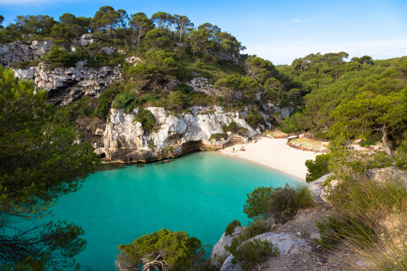 Bucht Cala en Turqueta auf Menorca mit türkisfarbenem Wasser, Sandstrand und bewaldeten Felsen