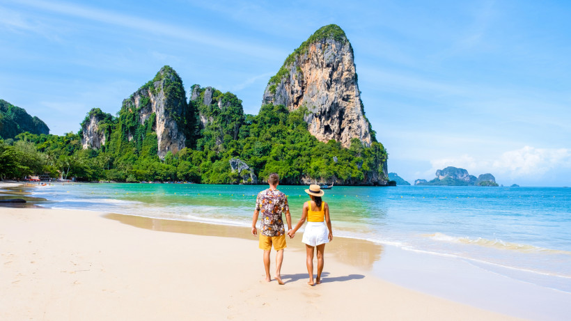 Railay Beach in Krabi, Thailand: Paar spaziert am weißen Sandstrand vor türkisfarbener Andamanensee und imposanten Kalksteinfelsen.