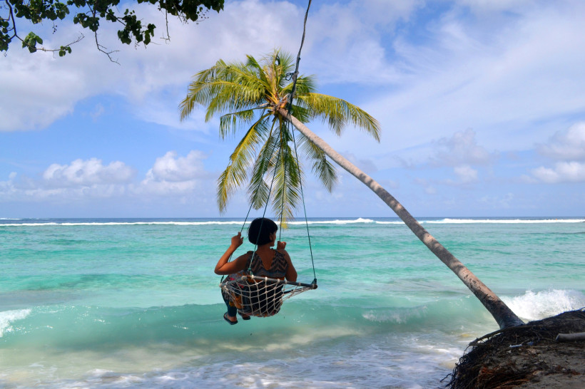 Malediven Person sitzt auf einer Schaukel unter einer Palme direkt am Strand der Malediven mit Blick auf das türkisblaue Meer