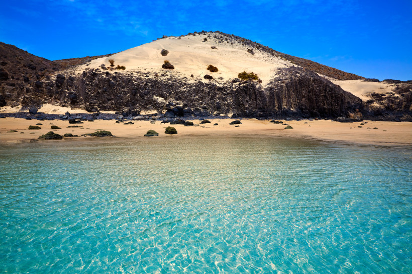 Küstenlandschaft bei Mal Nombre mit türkisfarbenem Wasser, Sandstrand und dunklen Felsformationen