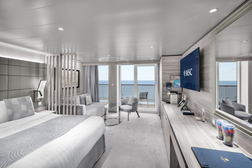 MSC World Europa – Yacht Club Deluxe Suite mit Balkon und Meerblick Yacht Club Deluxe Suite auf der MSC World Europa mit Doppelbett, Sitzbereich und Balkon mit Meerblick