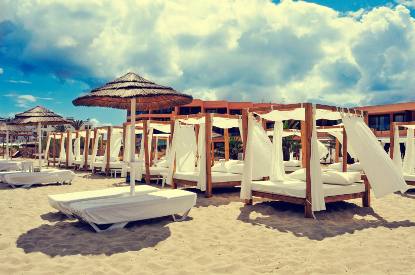 Sonnenliegen und Daybeds mit weißen Vorhängen im Beachclub an der Playa d’en Bossa